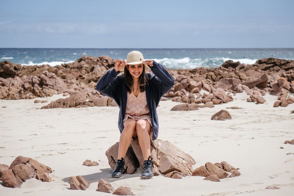 Temperatura en Australia chica joven encima de una roca sonriendo y sujetándose el sombrero